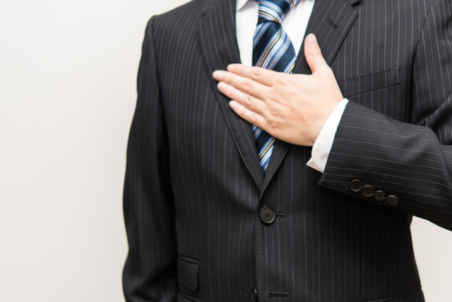 左手の掌を胸にあてているスーツ姿の男性